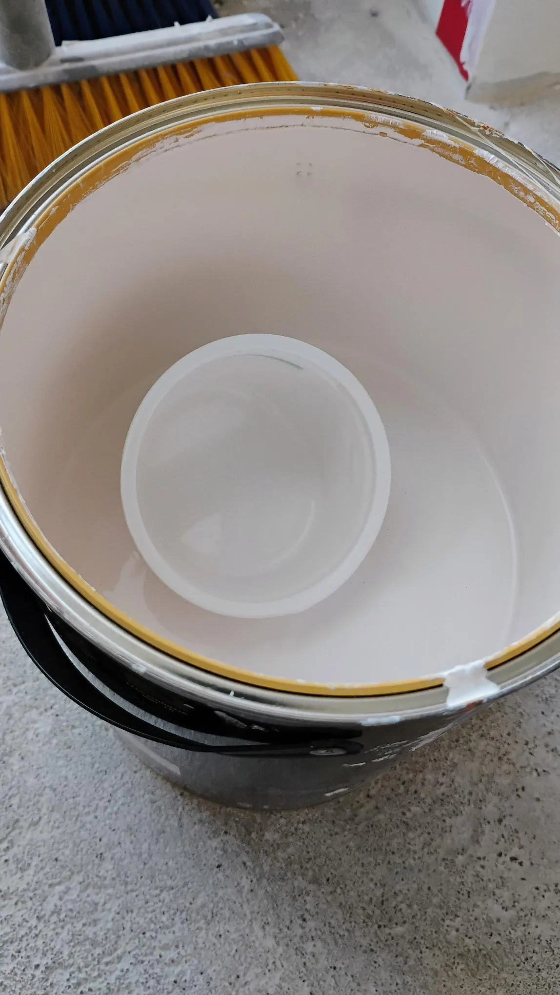 A cottage cheese tub lying in an open tin of white paint